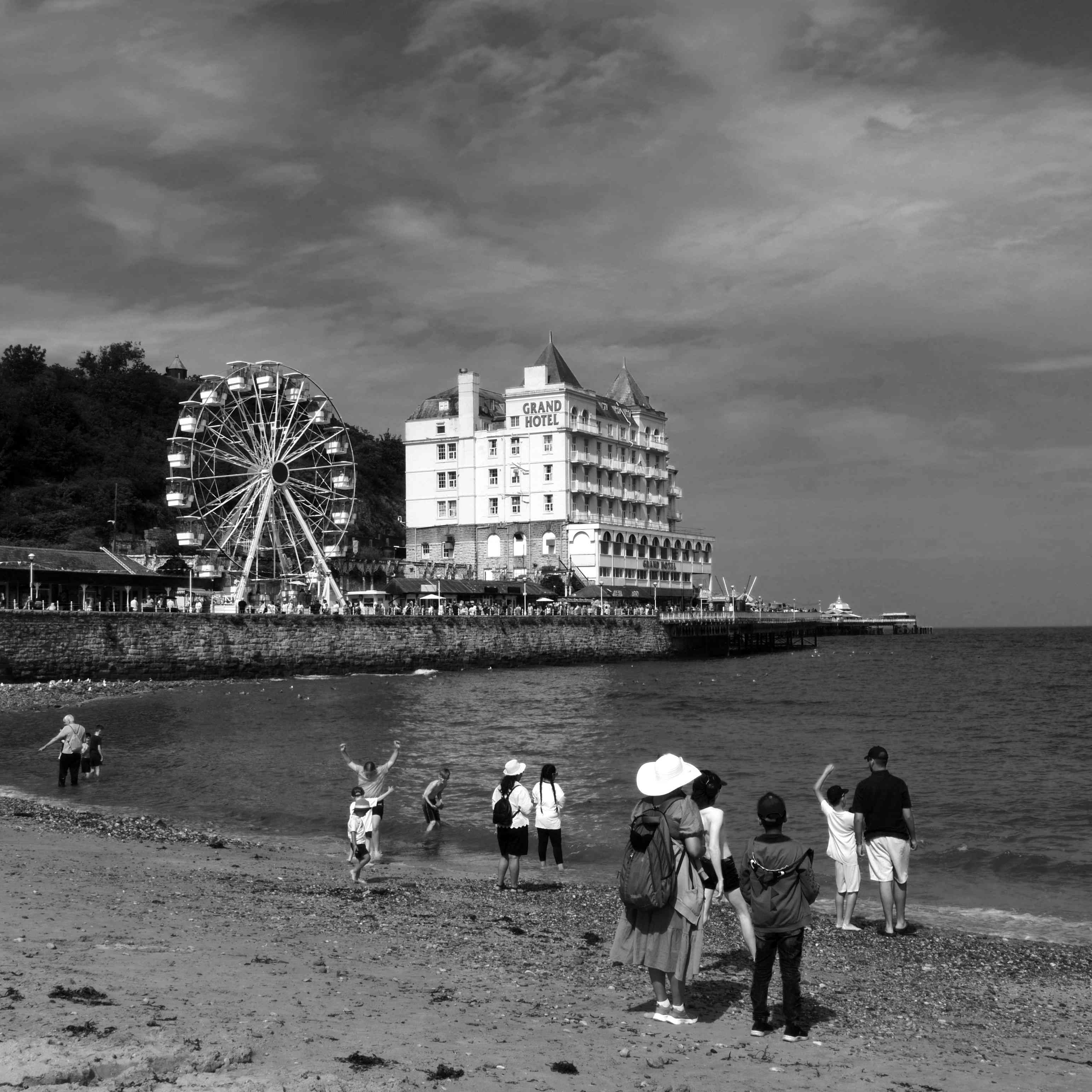 A beach scene with people by the shore, a ferris wheel, a hotel, and a pier in the background