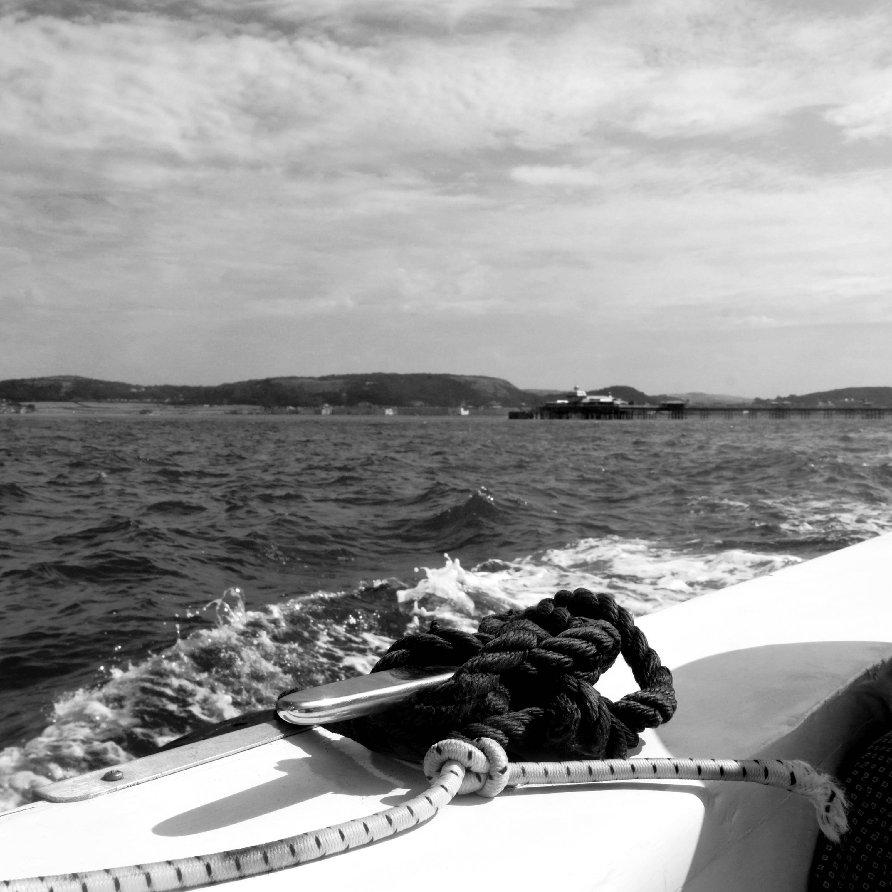 A view from on a boat, with a bit of rope tied in the centre on the side of the boat, and a distant shoreline visible behind.