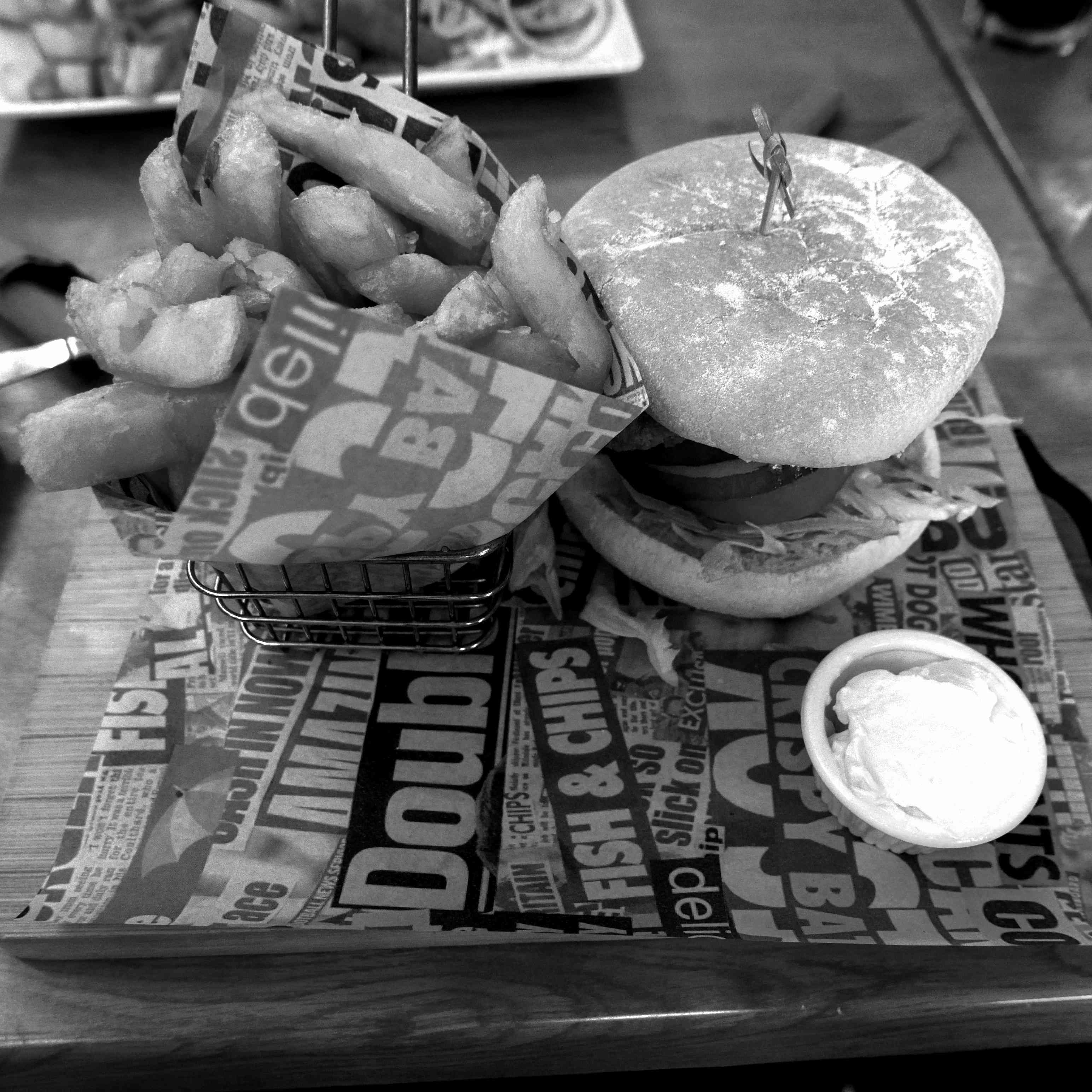 A basket of chips, garlic mayo dip, and a vegan burger, served on a board