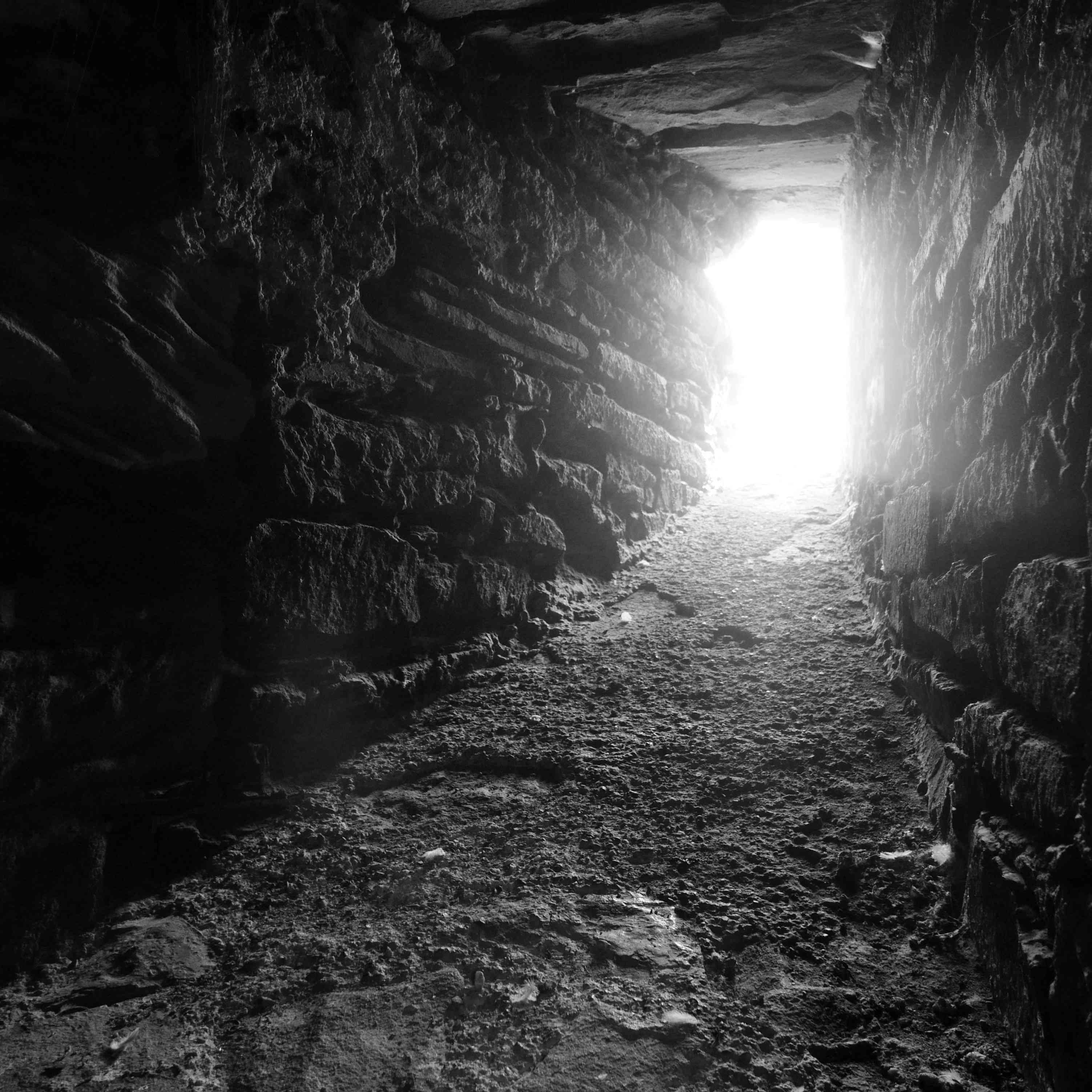 A high-contrast image of light streaming in through a narrow castle window, making long shadows on the coarse stone walls 