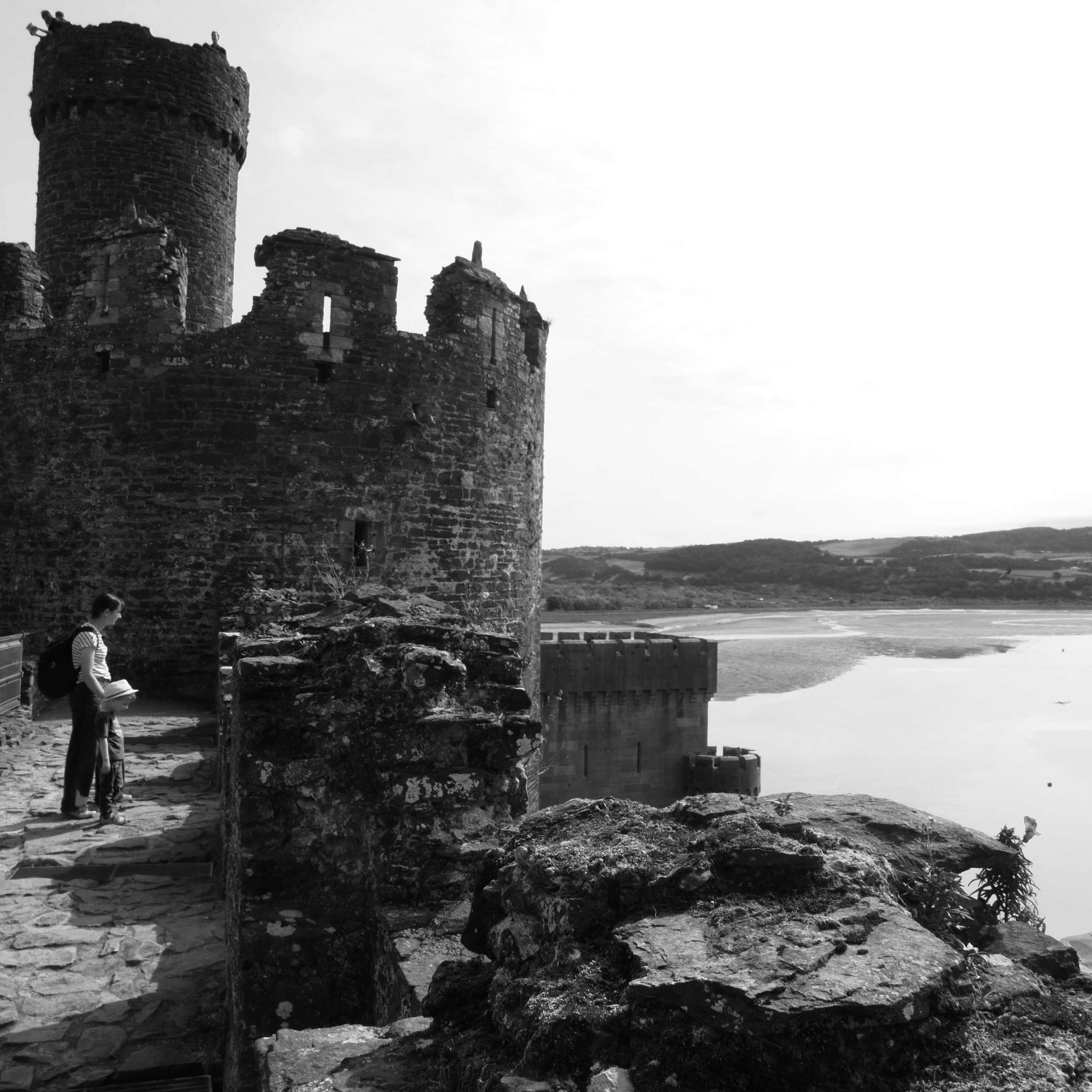 A boy and his mother looking over a castle wall at a river estuary. Towers are visible