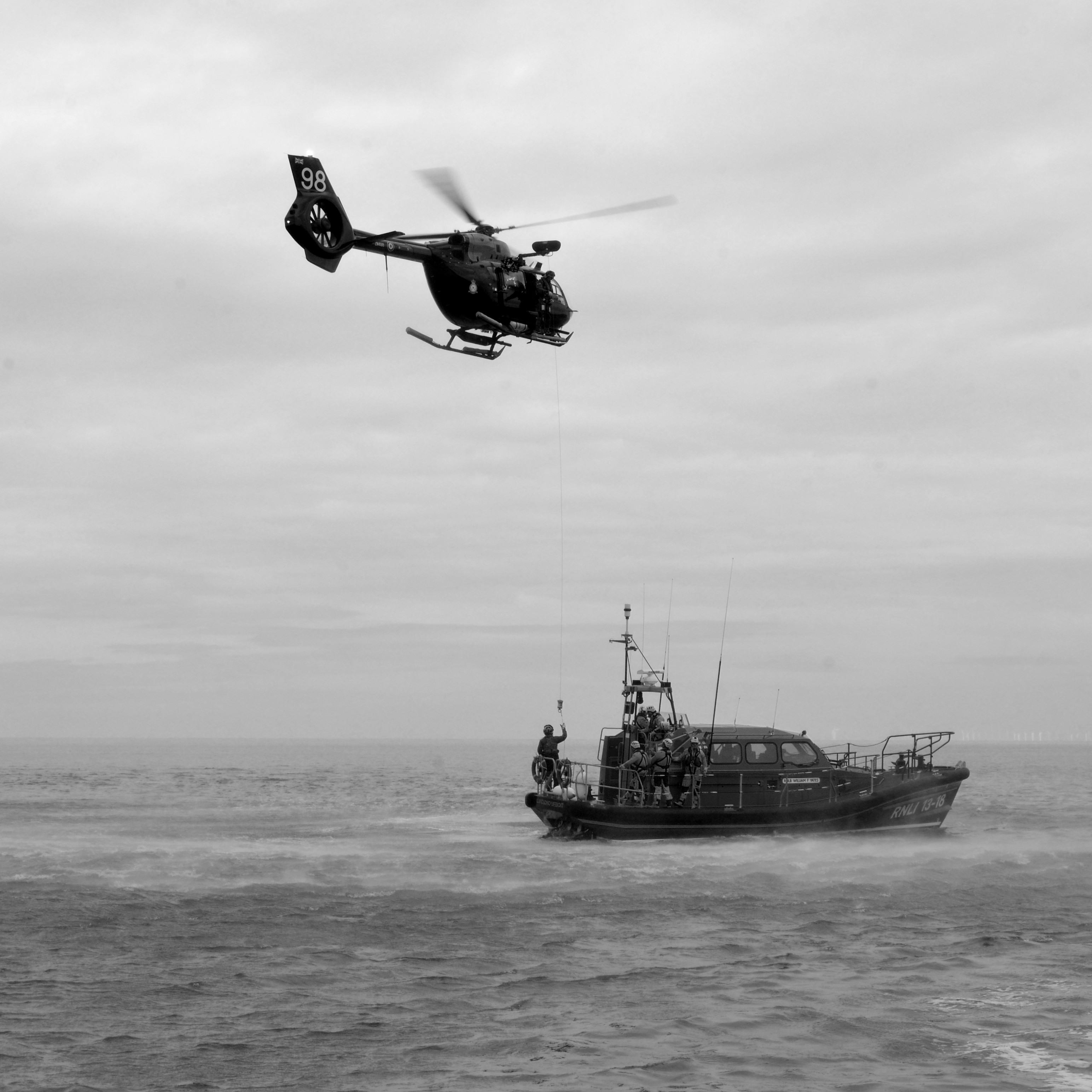 Lifeboat at sea and helicopter with a winch picking up a person from the boat