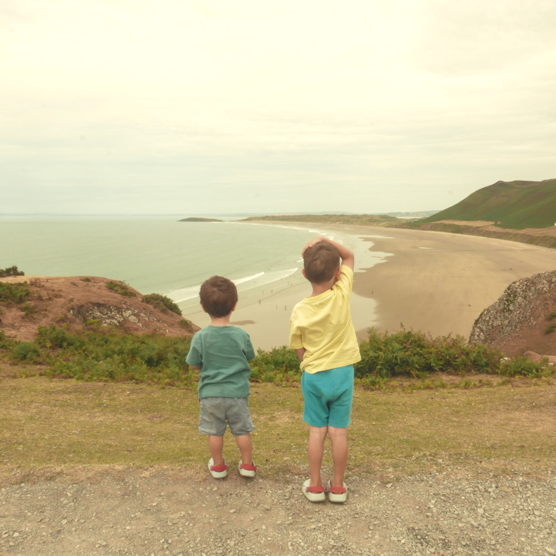 Two little boys in shorts and t-shirt, looking over a cliff onto a large bay.