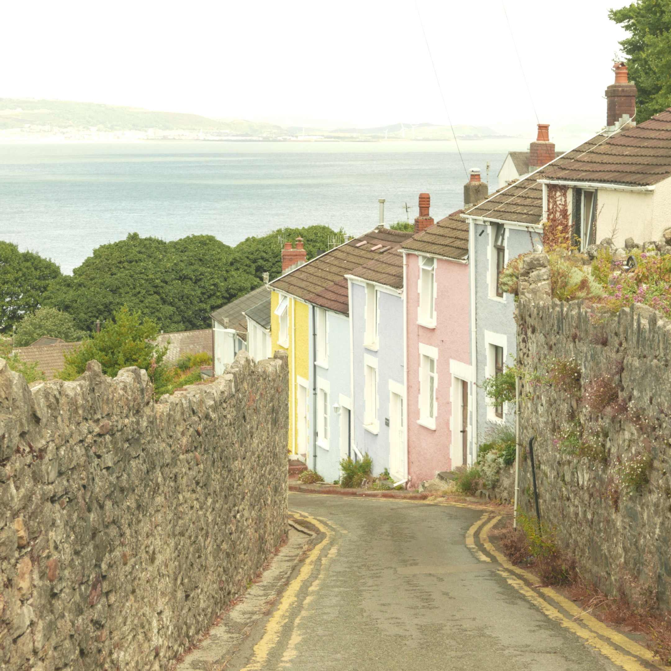 A steep narrow street with multicoloured painted cottages down one side.