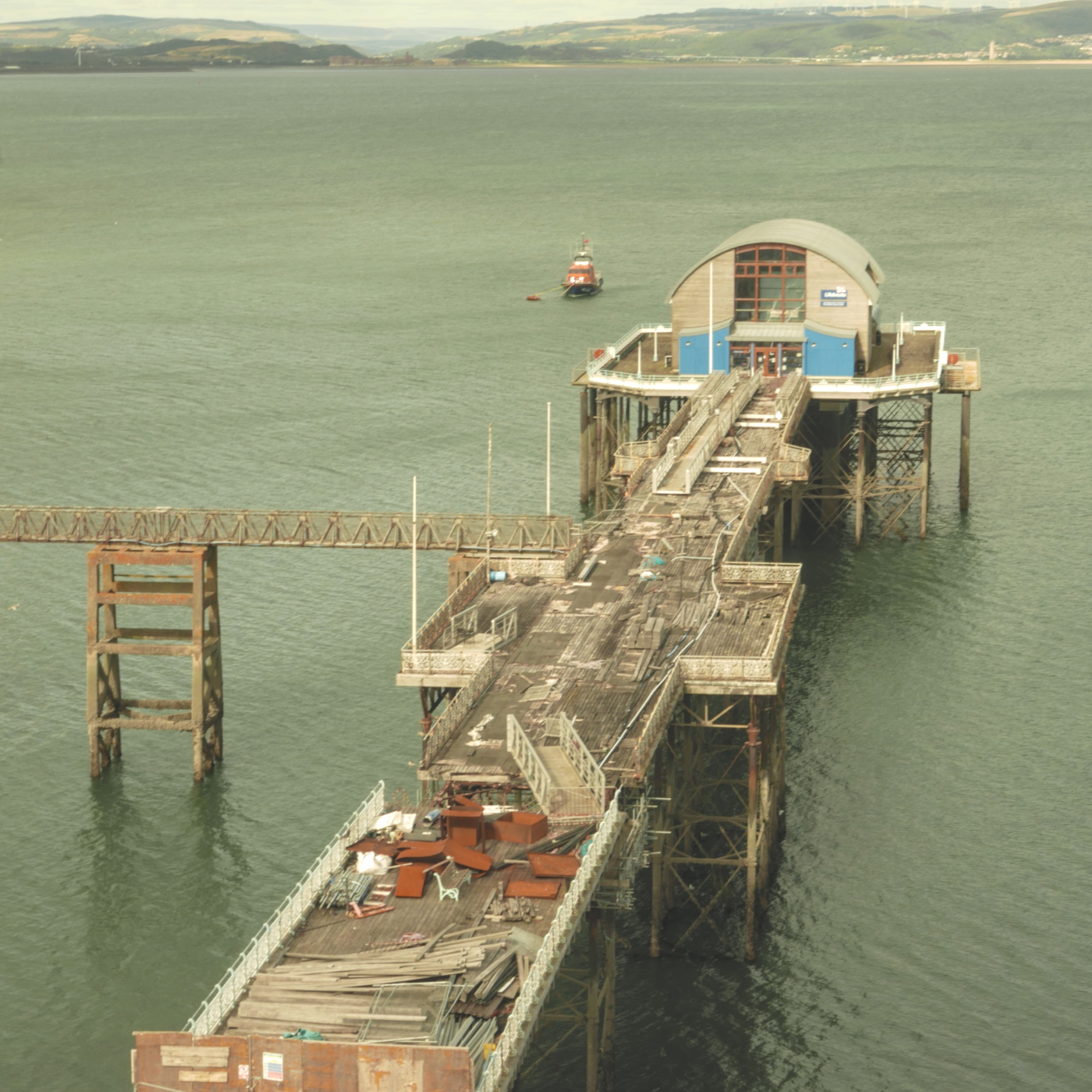 A pier with a lifeboat station at the end. The pier is in a state of disrepair.