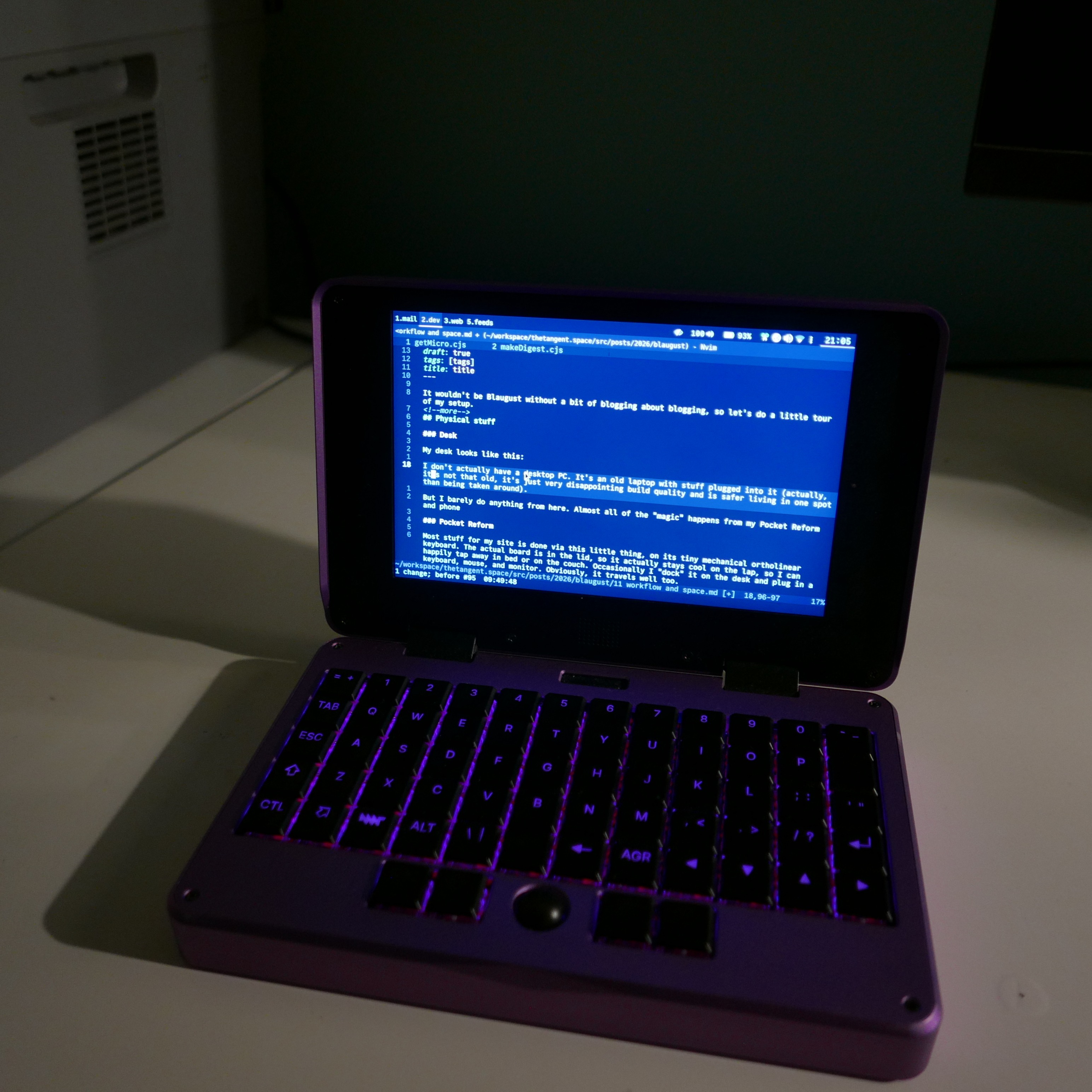 The Pocket Reform laptop with the lid open. The keys have purple backlights to match the metal purple shell, and are arranged in an ortholinear layout. The laptop has a trackball where the trackpad would usually be.