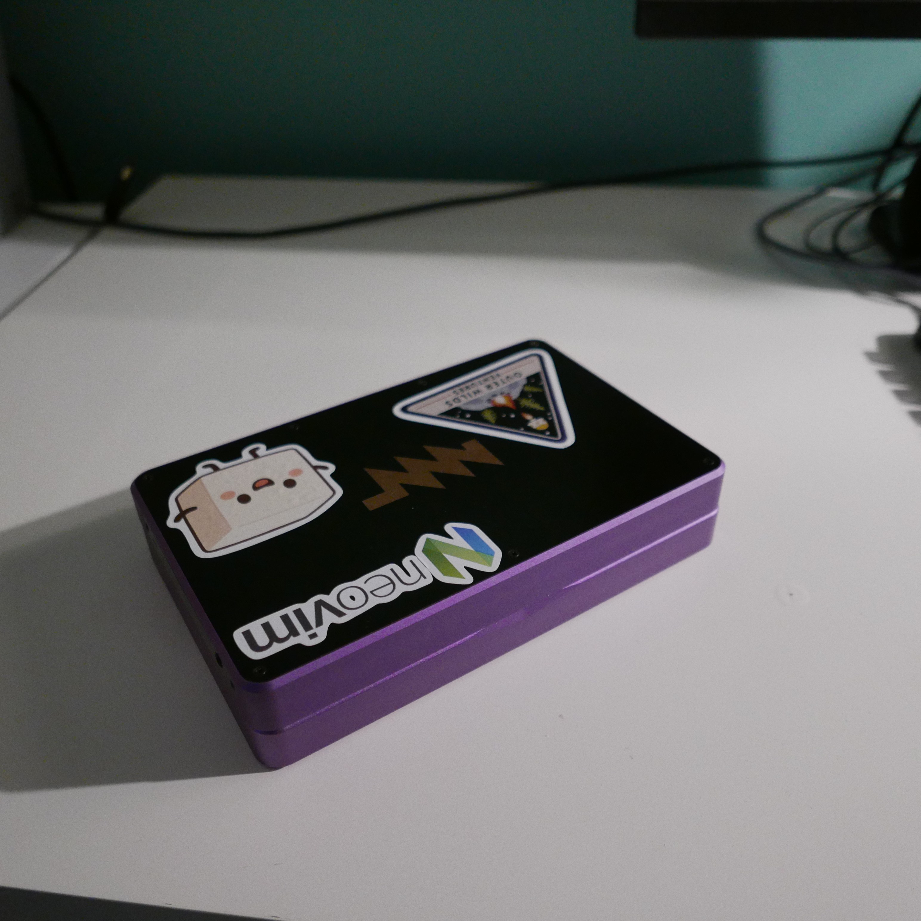 A chunky 7-inch laptop made of purple metal with a black plastic lid. Several stickers are visible on the lid.