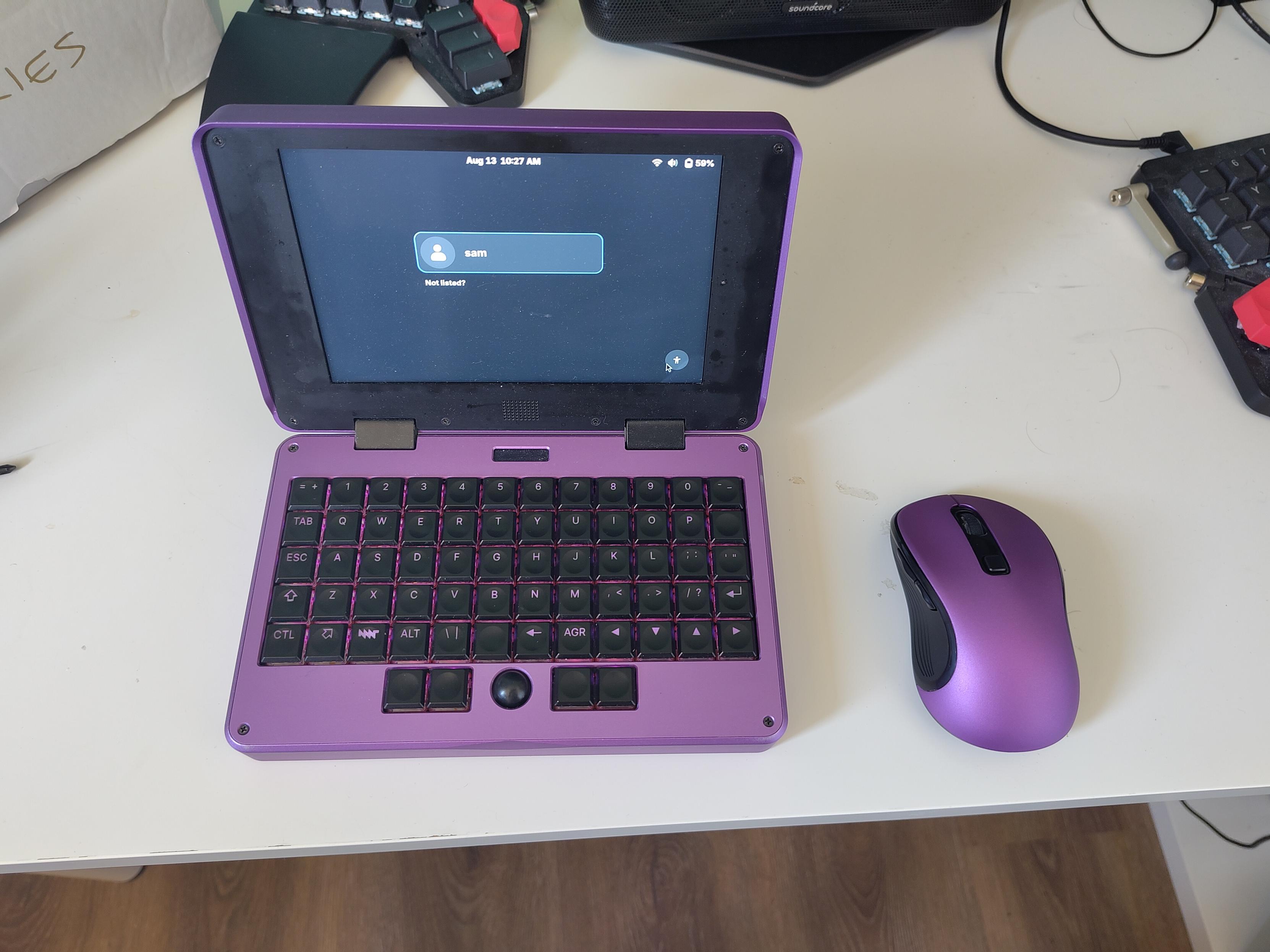 A photo of a purple mouse that nigh-on perfectly matches the purple body of the MNT pocket reform laptop